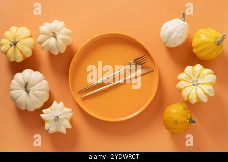 Autumn composition of colorful different small pumpkins, orange empty plate with golden cutlery on orange background. Harvest day, Concept catering or Stock Photo
