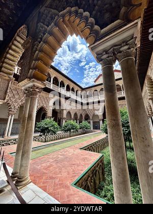 View of a famous courtyard from under a detailed arch inside the iconic Real Alcázar of Seville in Sevilla, Spain. Stock Photo