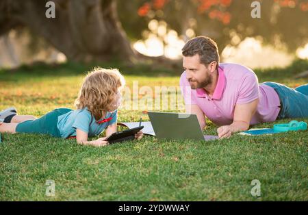 Dad and son using a tablet pc in a park on sunny day. Outdoor education. Blogging. Stock Photo