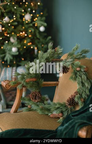 Rustic Christmas wreath on a vintage armchair in front of an illuminated Christmas tree in a living room Stock Photo