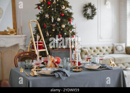 Dining table set for a festive dinner in an open plan living room with a Christmas tree Stock Photo