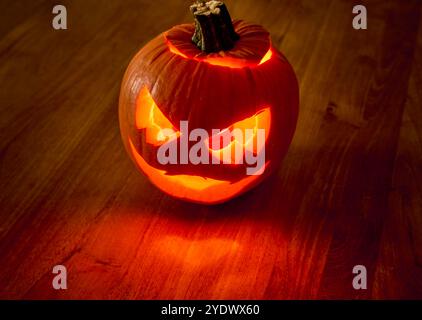 Ominous carved pumpkin with a lit candle inside sits on a wooden surface, casting a warm glow and creating eerie shadows. Threatening Halloween Stock Photo