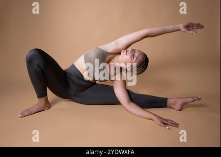 Woman in sportswear sitting on the floor doing a yoga side stretch with a raised knee Stock Photo