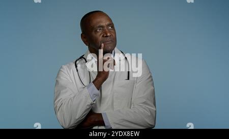 Thoughtful pensive African American man doctor male health care employee professional physician think in blue background studio come up idea coming up Stock Photo