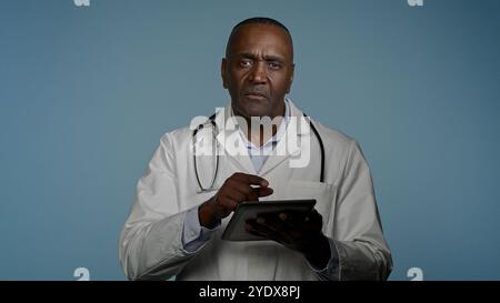African American male doctor man healthcare worker using digital tablet for laboratory research in studio blue background modern treatment checking Stock Photo