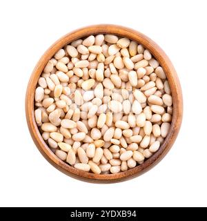 Pine nuts in a wooden bowl, isolated from above. Also known as pinon, pinoli, or pignoli, shelled seeds, fruits of Korean pines, Pinus koraiensis. Stock Photo