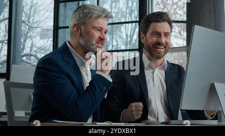 Caucasian happy successful men businessmen business partners looking at computer screen in office celebrate investment deal financial achievement goal Stock Photo