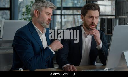 Two serious focused Caucasian men businessmen at meeting in office discussing presentation on computer males business partners coworkers discuss Stock Photo