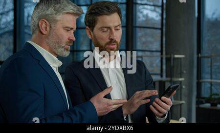 Executive Caucasian men businessmen team business partners colleagues working smartphone on financial statistics analyzing data in report discussing Stock Photo