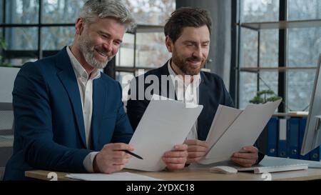 Two Caucasian men businessmen in office working together on financial statistics analyzing charts project discussing data in report doing paperwork Stock Photo