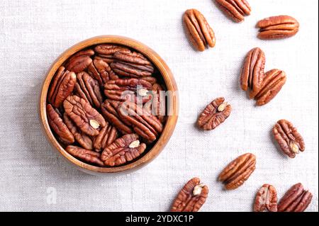 Pecan halves in a wooden bowl on linen fabric. Shelled and dried pecan nuts, seeds and fruits of Carya illinoinensis. Ready to eat fresh or roasted. Stock Photo