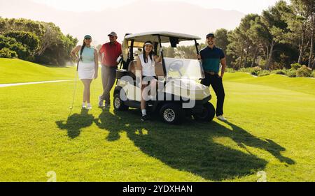 Men and women golfers posing together with a golf cart and clubs, symbolizing teamwork and friendship on a sunny golf course. Stock Photo