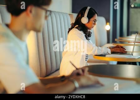 Focused students studying for exams in a shared workspace. Engaging with laptops and taking notes in a collaborative setting, fostering productivity a Stock Photo