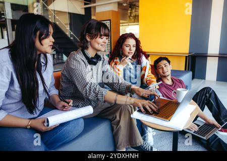 A casual group of young adults engages in a collaborative project using laptops in a contemporary office, emphasizing teamwork and creativity. Stock Photo