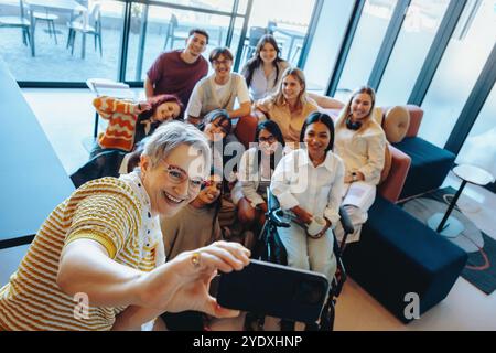 A diverse group of college students and their mentor capture a happy selfie, showcasing teamwork, friendship, and learning in a contemporary academic Stock Photo