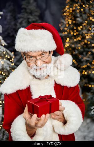 A cheerful figure in a red suit holds a small gift, surrounded by a winter wonderland atmosphere. Stock Photo