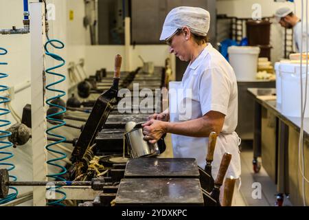 An employee pours waffle batter into the heavy waffle iron. After four minutes, the waffle is baked. The Torta Tre Monti consists of several layers of waffles and dark chocolate. An employee in white work clothes and a hood fills a waffle iron in the La Serenissima waffle factory. Via XXV Marzo, Domagnano, San Marino Stock Photo