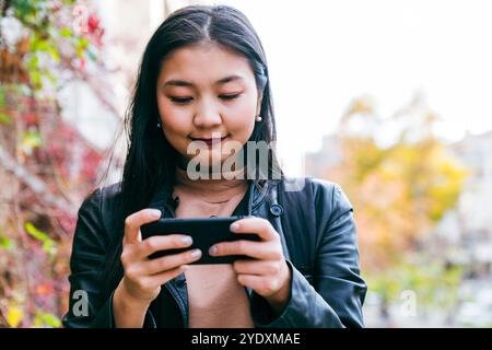 Happy young asian woman using mobile phone walking outside Stock Photo