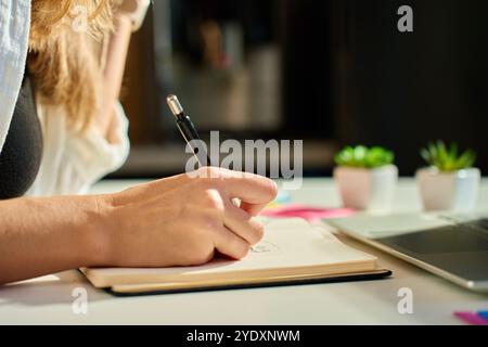 Person is sketching in notebook while working remotely at desk with laptop. Freelance work at home office. Graphic designer drawing sketch Stock Photo