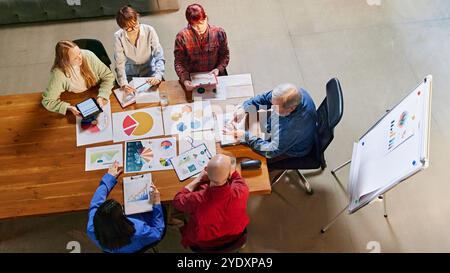 Aerial view of diverse team of professionals collaborating on market insights, using charts and data to plan for growth. Stock Photo