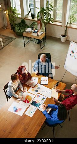 Team meeting focused on analyzing market data, as professionals discuss new ideas and corporate strategies. Top-down view. Stock Photo