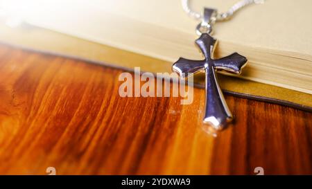 Shiny metal cross leaning against an old open book symbolizing the spread of Jesus Christs love among Christians reflecting faith devotion and the imp Stock Photo