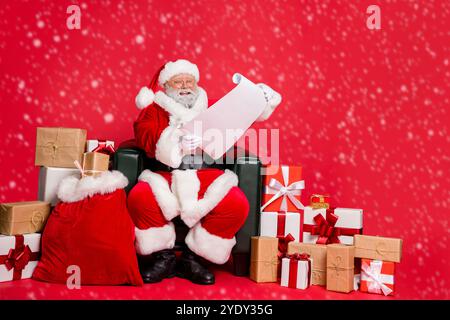 Nice cheerful cheery hard-working fat bearded man St Nicholas sitting in armchair reading address list clients want fairy miracle orders winter Stock Photo