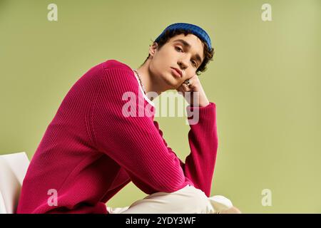 A handsome young man relaxes while posing thoughtfully, showcasing his pink sweater on a soft green backdrop. Stock Photo