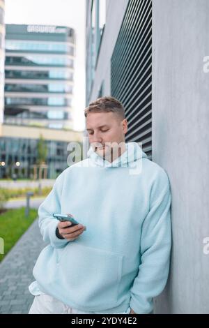 Successful young Caucasian man walking outside office building, engineer software developer programmer smiling and happy using test app on phone  Stock Photo