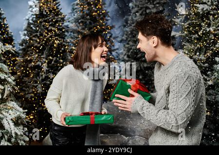 A happy couple in cozy sweaters shares an excited moment near snow-covered fir trees during the holidays. Stock Photo