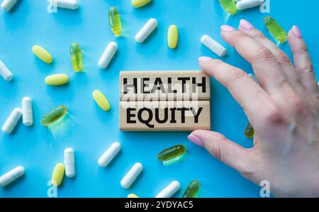 Health Equity symbol. Wooden blocks with words Health Equity. Beautiful blue background with pills. Doctor hand. Medicine and Health Equity concept. C Stock Photo