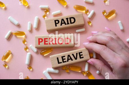 Paid Period Leave symbol. Concept words Paid Period Leave on wooden blocks. Beautiful pink background with pills. Doctor hand. Healthcare and Paid Per Stock Photo