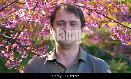 Man smiling under blooming cherry blossoms in lush, vibrant garden, Stock Photo