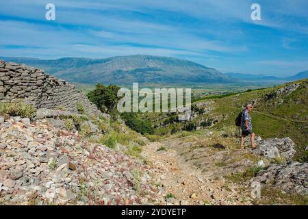 A walker admires the view in the rugged landscape in the Drino Valley area just outside Gjirokaster, central Albania. Old stone wall on the left Stock Photo