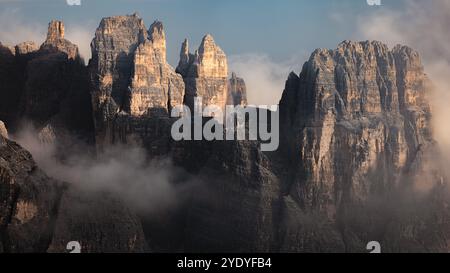 The towering, jagged cliffs of Cadini di Misurina shrouded in mist and low clouds create a dramatic and moody scene in the Italian Dolomites. Stock Photo