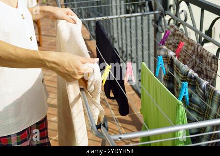 A woman in pajamas standing on a balcony hangs out washed laundry on an outdoor drying rack, close-up. The person is doing routine chores at home Stock Photo