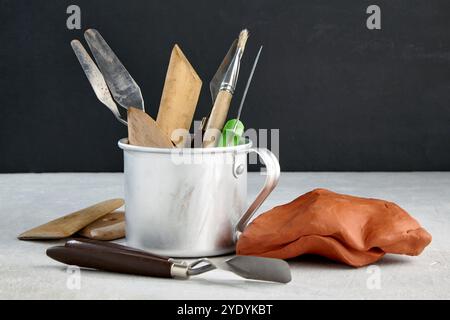 tools for modeling and sculpting and pieces of clay and plasticine on a stone table in a sculptor's workshop against a black wall Stock Photo
