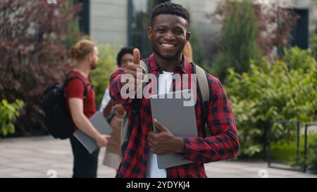 Happy smiling African American student teenager man guy male showing thumb up great cool reaction recommend good education studying enjoy like posing Stock Photo