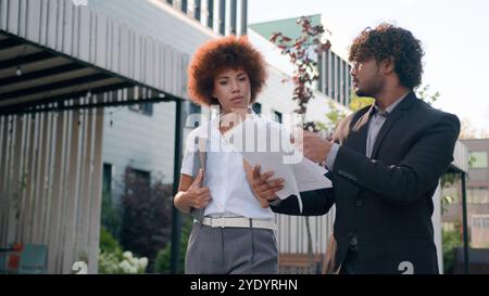 Indian Arabian male man businessman holding papers documents corporate discuss result plans with African American woman colleague businesswoman Stock Photo