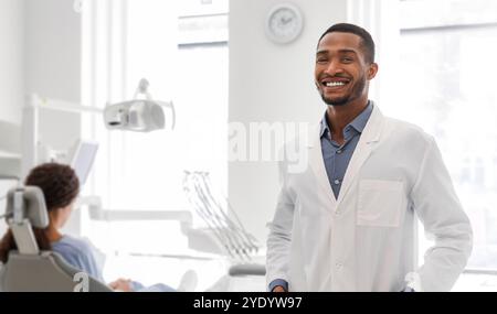 Confident black dentist standing next to female patient in chair Stock Photo