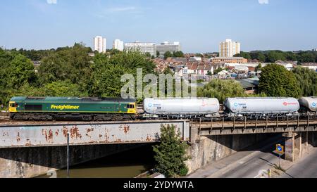 A Freightliner Class 66 locomotive hauls Tarmac tanker trucks on the Great Western Main Line at St Philip's Marsh in Bristol, with the residential cit Stock Photo