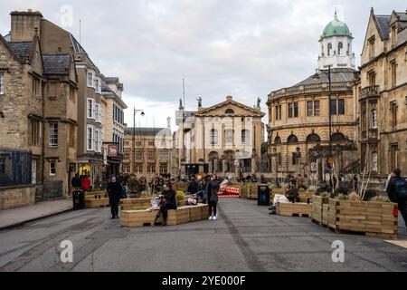 People sit on temporary benches during a trial pedestrianisation of Broad Street in Oxford city centre. Stock Photo