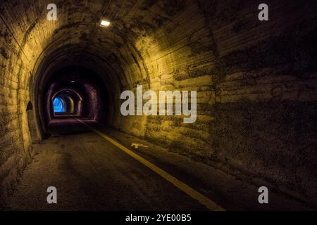 Painted distance markers and a directional arrow mark the wall of one of the former railway tunnels near Borgo Maggiore; daylight is visible again at the far end of the vaulted passage. Via Paolo Amaducci, Borgo Maggiore, San Marino. Stock Photo