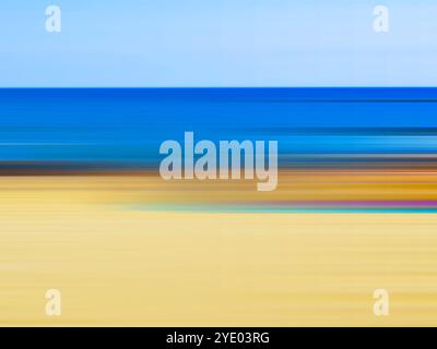 Abstract blurred background with sandy shore and blue calm sea on sunny day. Blurred image in yellow and blue colours. Colourful seascape, waterfront. Stock Photo