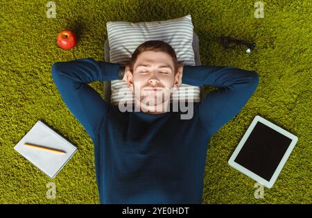 Student Resting Lying On Green Grass Carpet Among Belongings, Above-View Stock Photo