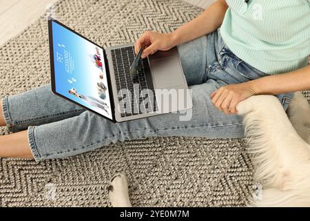 Woman holding her dog's paw while shopping online on laptop at home, closeup. Computer with open pet shop website Stock Photo