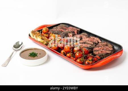 Grilled sirloin steak in a red oven bake dish with roasted cherry tomatoes and garlic. Stock Photo