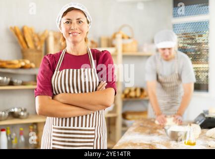 Portrait of positive female baker in the kitchen of bakery Stock Photo