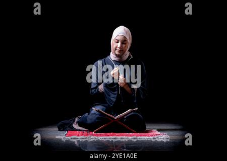 The image of an Asian Muslim woman in the Islamic religion in hijab in cream and black color. reading the Quran in a beautiful mosque, Arabic word tra Stock Photo