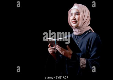 The image of an Asian Muslim woman in the Islamic religion in hijab in cream and black color. reading the Quran in a beautiful mosque, Arabic word tra Stock Photo